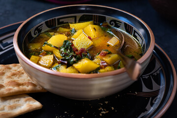 Vegan potato and beet greens soup served in ceramic bowl, along with crackers