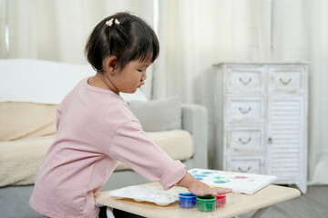 Asian Girls learn before going to school, engaging in a fun painting at home, dipping fingers into...