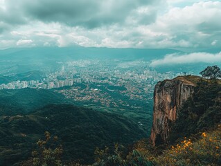 Naklejka premium Scenic Overlook of City From Rocky Cliff With Cloudy Sky and Greenery Below