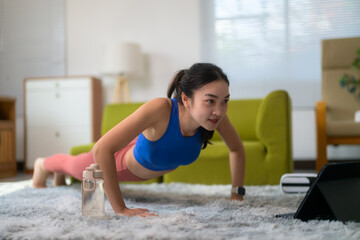 Fit athletic woman doing pushups training muscles at home watching online fitness videos on a tablet