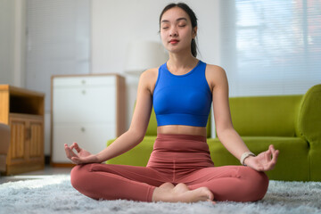 Fototapeta premium Relaxed asian woman practicing yoga, meditating in lotus position at home, enjoying peaceful morning