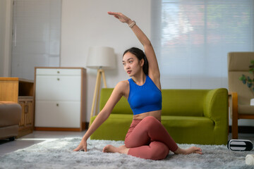 Fit sporty young asian woman doing yoga stretching exercises training at home in living room, watching online workout tutorials on laptop