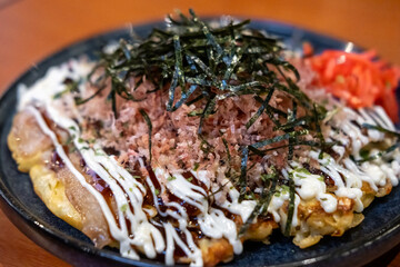 Okonomiyaki, a Japanese pizza or pancake containing a variety of ingredients served on plate with dried seaweed and dried bonito flakes