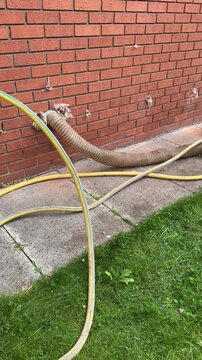 Vertical video. Old insulation extraction from external wall works scene. Small hose inserted into the external wall for blowing air in and old cavity insulation material is forced to move out.