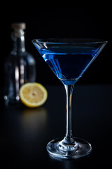 Blue cocktail in martini glass with lemon on black background