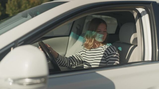 Cute Caucasian woman with blonde hair getting into her car. Fastening seatbelt with calm expression. Busy female in striped sweater preparing for drive to work. Using vehicle for faster travel.