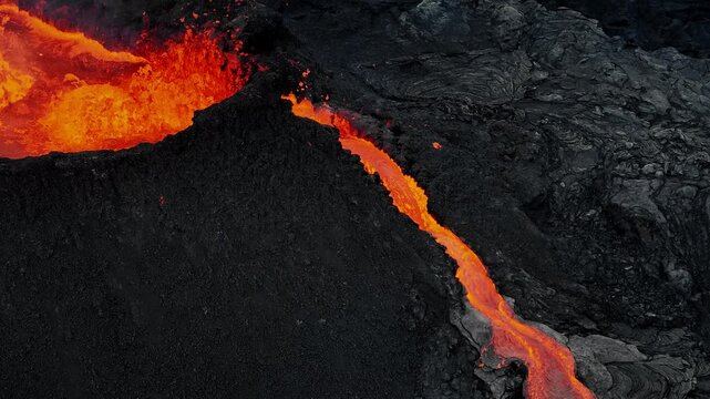 Erupting volcano, red hot magma boiling and splashing out a crater, making lava flows, drone close up shot. Concepts of volcanic activity, climate change, and nature.