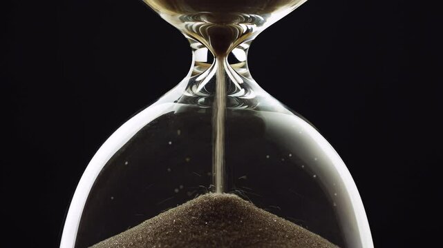 Sand running out in an hourglass, golden sand grains flowing through the glass device, timelapse shot. Time, and urgency concept.