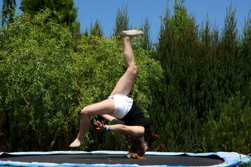 A young girl skillfully performing an impressive backflip on a trampoline in the sun
