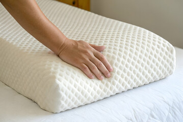 stress management, A hand gently presses down on a textured memory foam pillow on a bed, showcasing comfort and support for restful sleep.