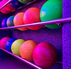 Colorful bowling balls resting on metal rack in illuminated bowling alley