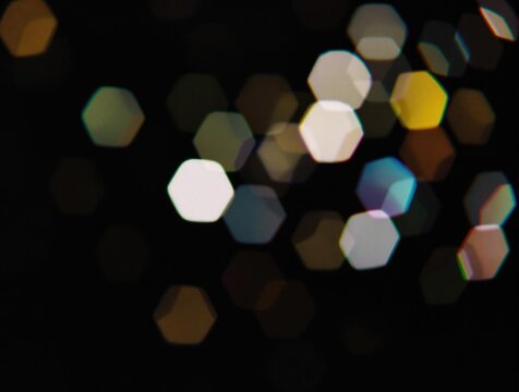 Colourful hexagonal bokeh light overlay with blurred geometric pattern, film grain effect on a dark backdrop