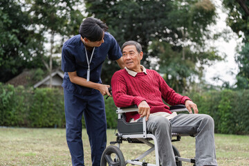 Caregiver lovingly engaging with elderly man in wheelchair under a green canopy in a garden
