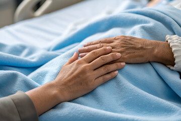 A gentle hand holds an elderly person's hand, symbolizing care and support in a hospital setting.