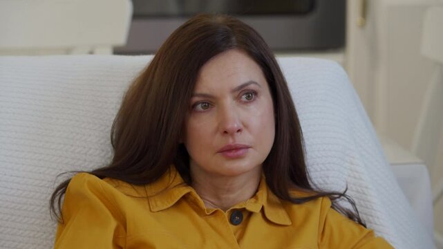 Impressionable woman sitting on sofa in living room in front of TV watching melodrama. Tear stained face of worried woman while watching movie.