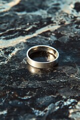 Close-up of a silver ring on a textured dark surface.