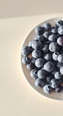 A vibrant display of fresh blueberries on a white plate, showcasing their deep blue hue and...
