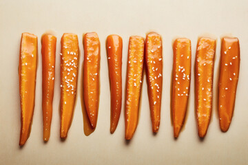 Top view of caramelized carrots glazed in honey, on a monochromatic orange surface. Glossy glaze with sesame seeds.