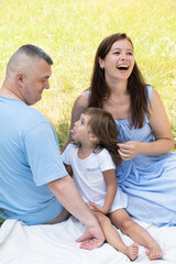 Obraz premium Mom, dad and daughter having fun on a picnic. Family vacation in nature