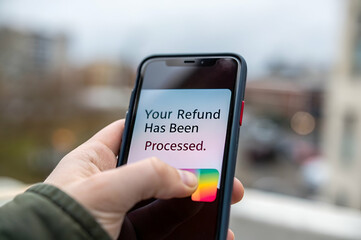 Customer Experience, A person holds a smartphone displaying a notification that their refund has been processed, set against an urban backdrop.