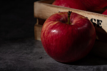 Close-up of a fresh red apple in dramatic moody lighting, placed on a dark stone surface with a rustic wooden crate in the background.