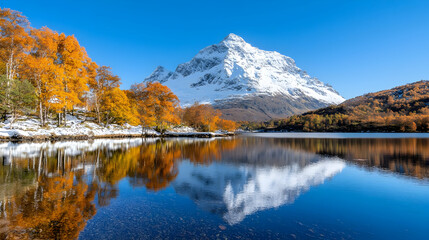 Naklejka premium Snow-capped mountain peak reflects in a calm alpine lake surrounded by colorful autumn trees under a clear blue sky.
