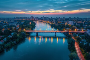 Naklejka premium Stunning aerial view of a city skyline at sunset with a shimmering river and illuminated bridge.