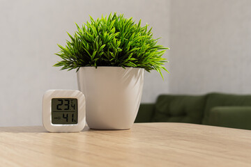 Small digital indoor temperature and humidity meter. Temperature sensor in living room. Small display and artificial plant on wooden table. Copy space