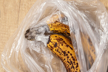 Overripe rotten bananas in a bag on wooden table. White mold on bananas