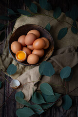 Brown chicken eggs in round wooden bowl, one egg is broken, perfect for Easter, natural light 