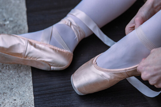 Closeup of a ballerina sitting on the floor adjusting pointe shoes. Ballet dancer putting ondance shoe onto her feet before performing