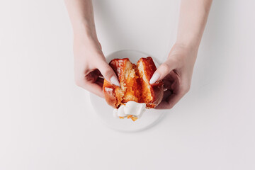 Woman's hands tearing, unwrapping, and crushing a pastry on a white plate against a white background