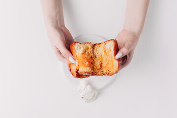 Woman's hands tearing, unwrapping, and crushing a pastry on a white plate against a white background