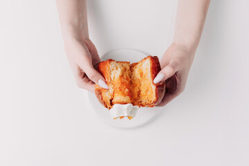 Woman's hands tearing, unwrapping, and crushing a pastry on a white plate against a white background