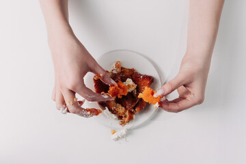 Woman's hands tearing, unwrapping, and crushing a pastry on a white plate against a white background
