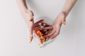 Woman's hands tearing, unwrapping, and crushing a pastry on a white plate against a white background