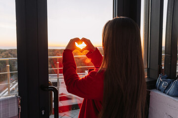Woman in a red blazer holding hands in a heart shape with sunlight shining through