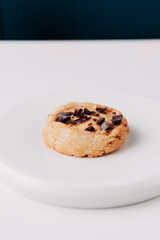 Round cookie with chocolate crumbs on a white plate against a white background