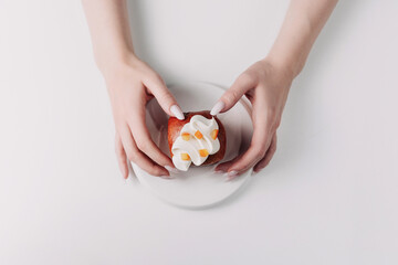 Woman's hands holding a pastry on a white plate against a white background
