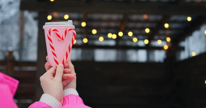 Winter pavilion glows behind pink cup and candy cane heart, where lights glitter against cool backdrop, letting lights enhance holiday mood, as lights underscore cheerful romance in frosty air.