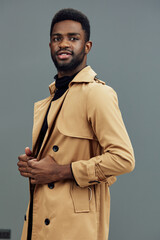 Stylish young man in a beige trench coat against a gray background, showcasing confidence and...