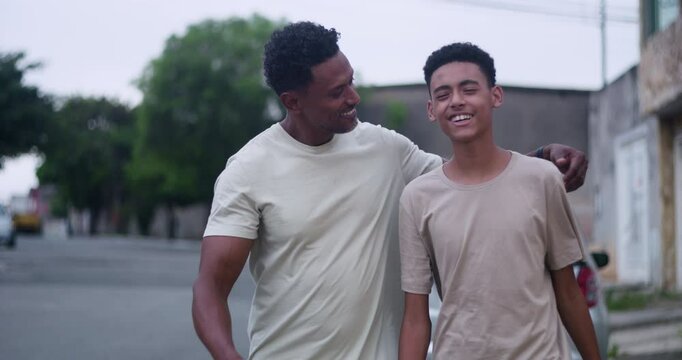 Father and teenage son of African descent standing side by side with bright smiles, father’s arm resting on son’s shoulders, sharing a joyful and proud family moment