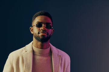 Fototapeta premium Confident young man in sunglasses and stylish beige jacket against a colorful gradient background, showcasing modern fashion and self assured attitude