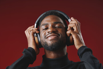Smiling young African American man wearing headphones, enjoying music against a vibrant red...
