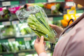 Fresh lettuce in plastic packaging held by shopper in grocery store, surrounded by various...