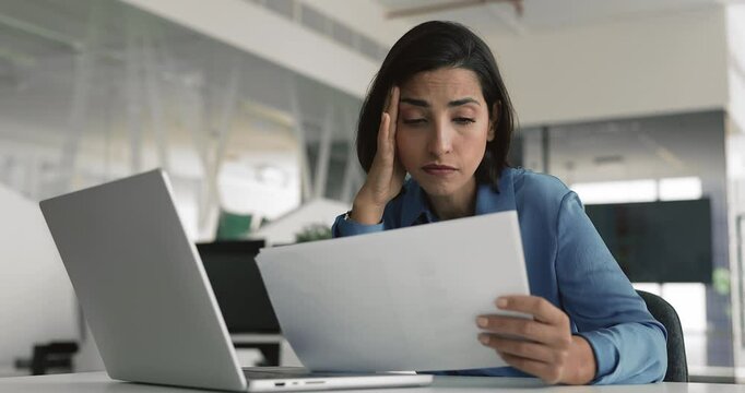 Office employee feels concerned while reads document with negative news, review sales data with revenue decrease, information about demotion, downsizing, or layoffs, unsuccess in work-related matter