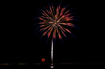 A vibrant firework explosion lights up the night sky over water