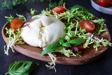 Creamy burrata cheese, made from mozzarella, is presented on a wooden plate.