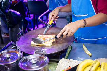 Street vendor preparing traditional Thai banana roti on a hot griddle at a bustling night market, showcasing authentic flavors and culinary skills