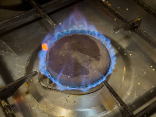 A stove with a burning blue gas burner, showing a dirty metal disc.